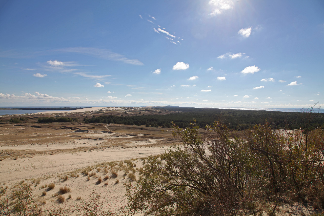 Atop the Parnidžio kopa sand dune and looking southward from the Lithuanian portion and toward the Russian portion of the Curonian Spit, visible, if only barely, to the viewer's left is the Kuršių marios – Kuršu joma – Curonian Lagoon – Куршский залив – Kurisches Haff and to the viewer's right the Baltijos jūra – Baltijas jūra – Baltic Sea – Балтийское море – Ostsee.